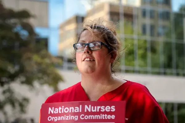 photo of kerri wilson wearing a red shirt and holding a protest sign