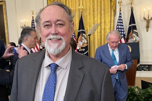 photo of Tim Greene wearing a gray suit and blue tie standing inside the White House