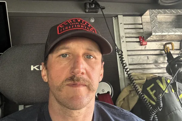 photo of Welcker Taylor wearing a hat and t-shirt that read Asheville Firefighters Local 332 and sitting in the cab of his fire truck