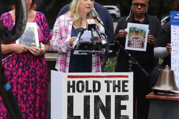 photo of Gianna Polito speaking at NC Workers Memorial Day service behind a sign that reads "hold the line for safe jobs"