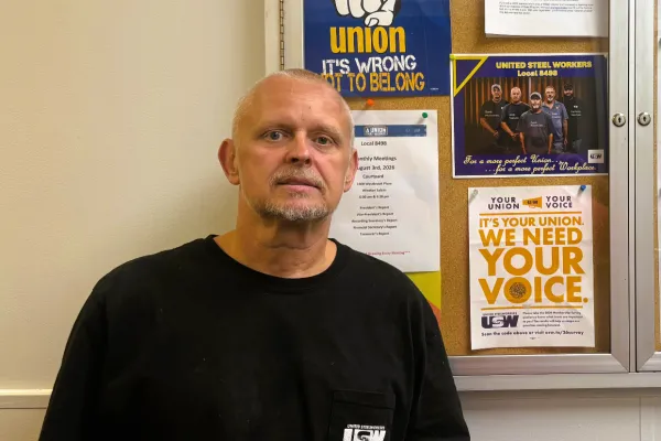 photo of Jason Gentle wearing a black USW shirt at work standing in front of a case displaying union posters
