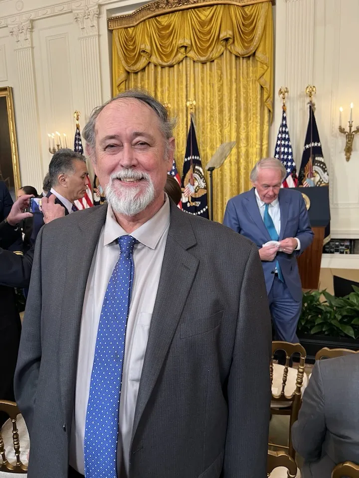 photo of Tim Greene wearing a gray suit and blue tie standing inside the White House