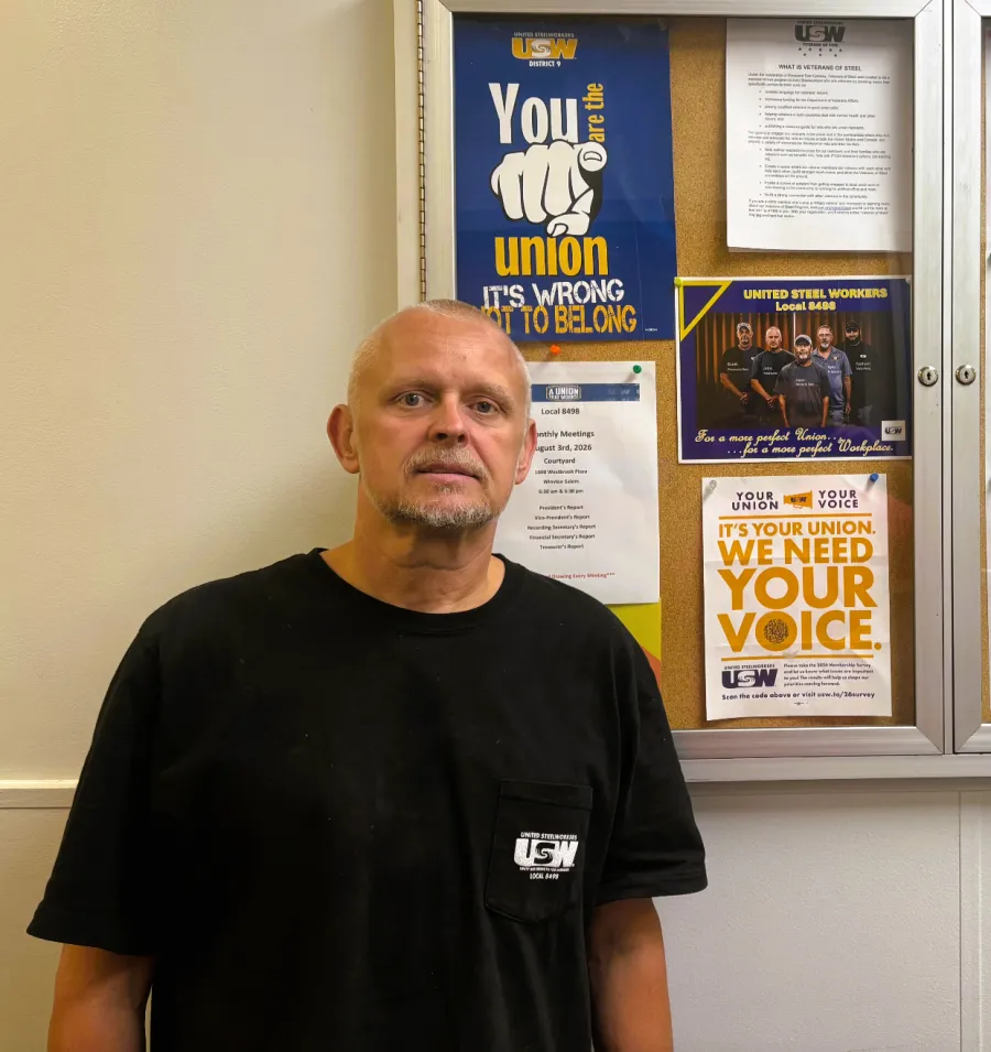 photo of Jason Gentle wearing a black USW shirt at work standing in front of a case displaying union posters